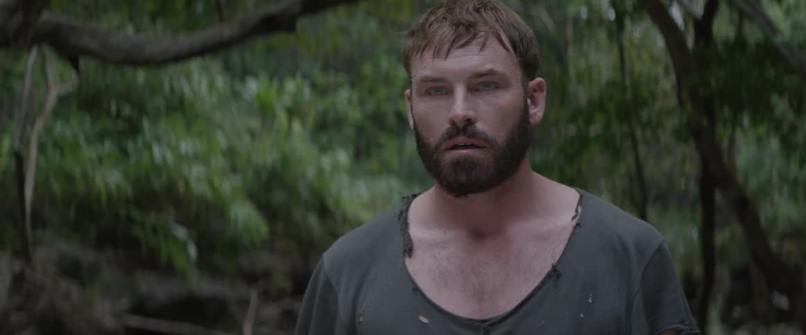 A man walks in a forested area while wearing a tattered shirt