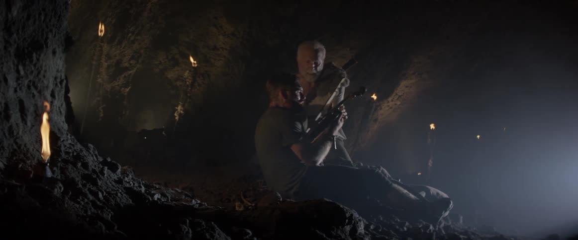 Two men are in a dark cave with a violin
