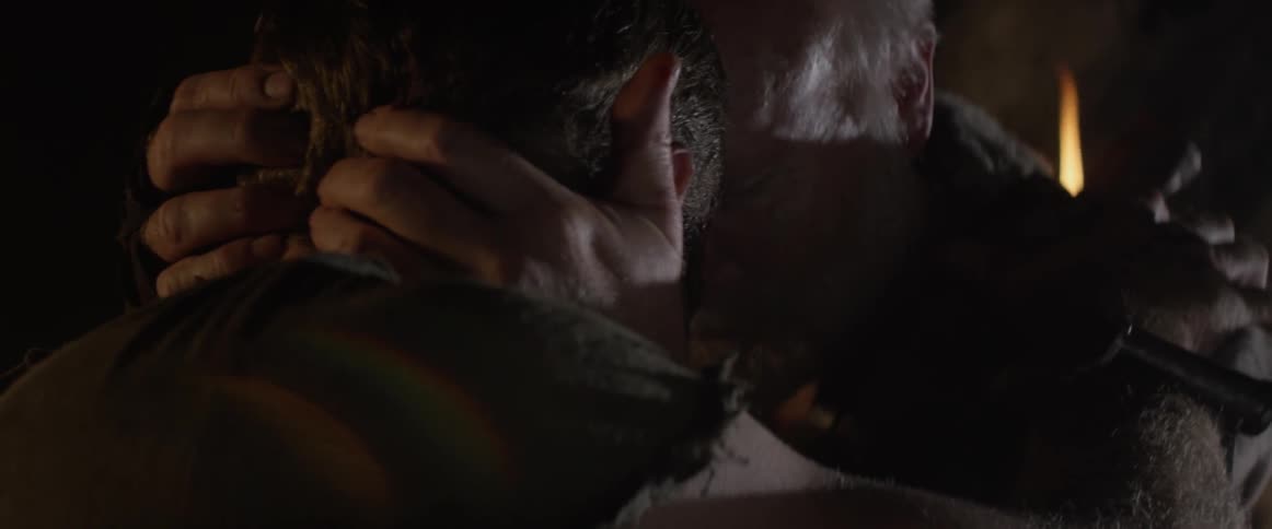 Two men hug in a dark cave