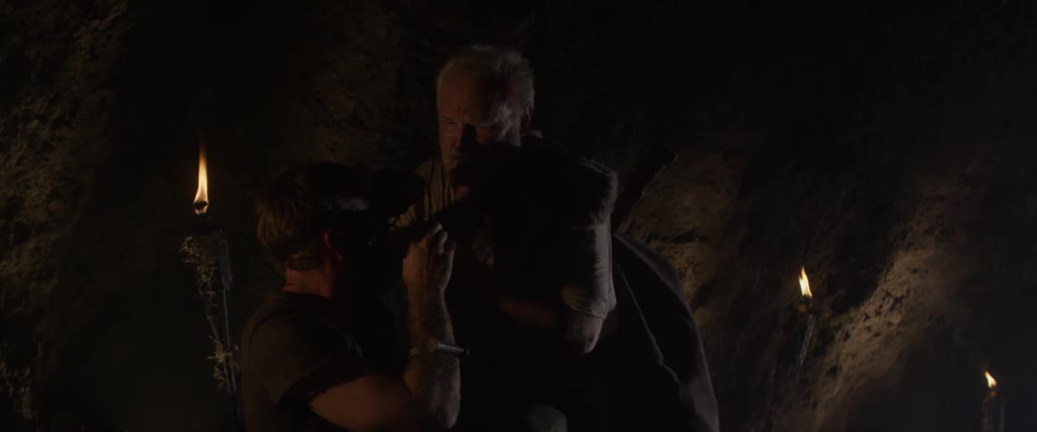 An elderly man consoles a young man in a cave