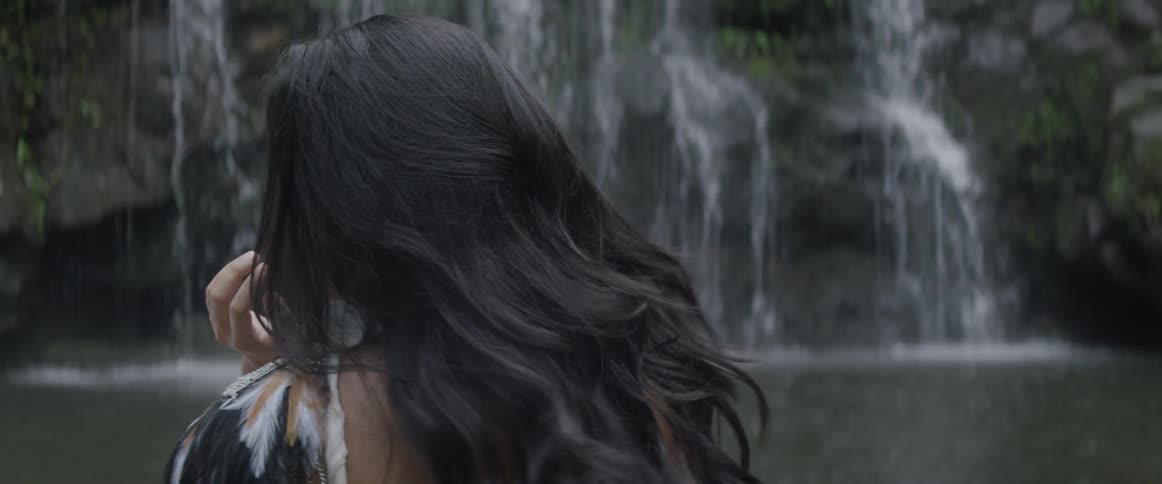 A woman taking off her shirt next to a waterfall and looking at the camera smiling