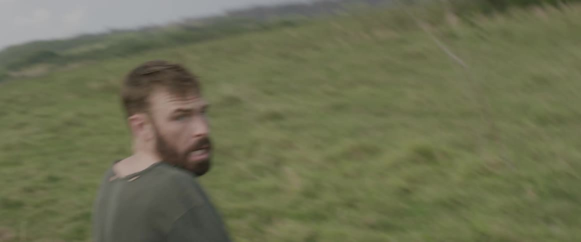 A man races across the green grass on a cloudy day