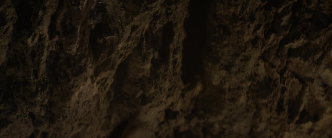 A man pulls a chain out of a rock wall in the dark