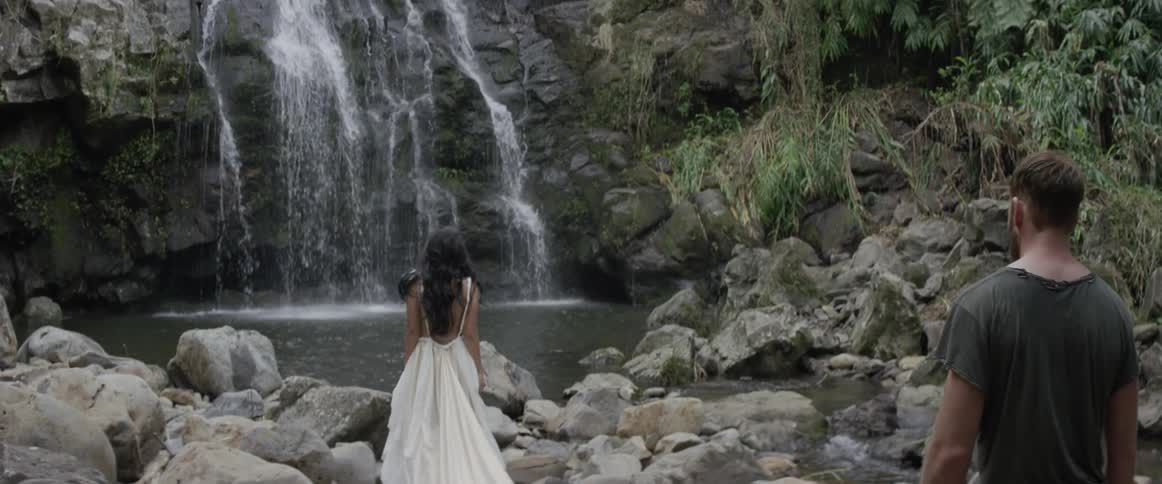 A waterfall is splashing as a woman and man walk towards it