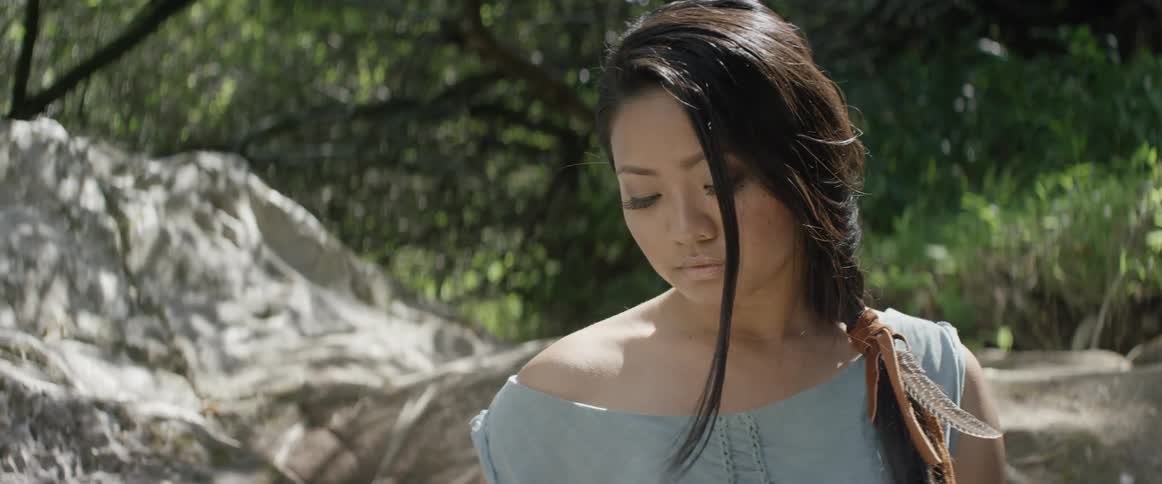A woman stands outside under trees as the sun shines