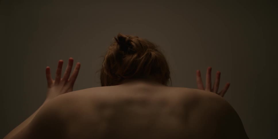 A naked woman is flexing her arms and arching her shoulders