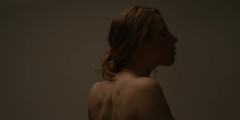A woman not wearing a shirt sits up and slowly turns to look behind her