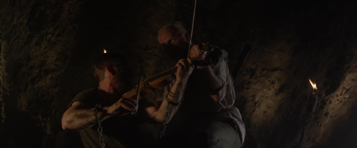 Two men play violins inside a cave