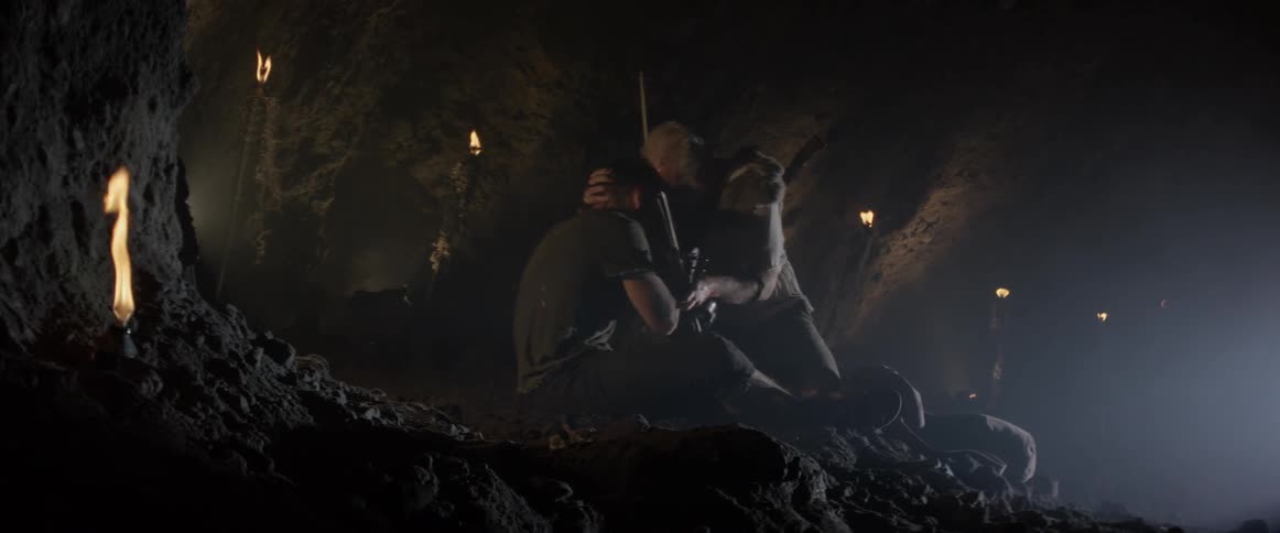 A man embraces another while they sit on a cave floor