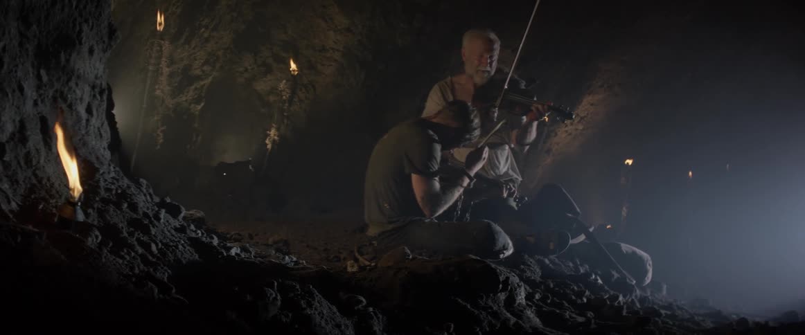 Two men are sitting in a cave playing the violin