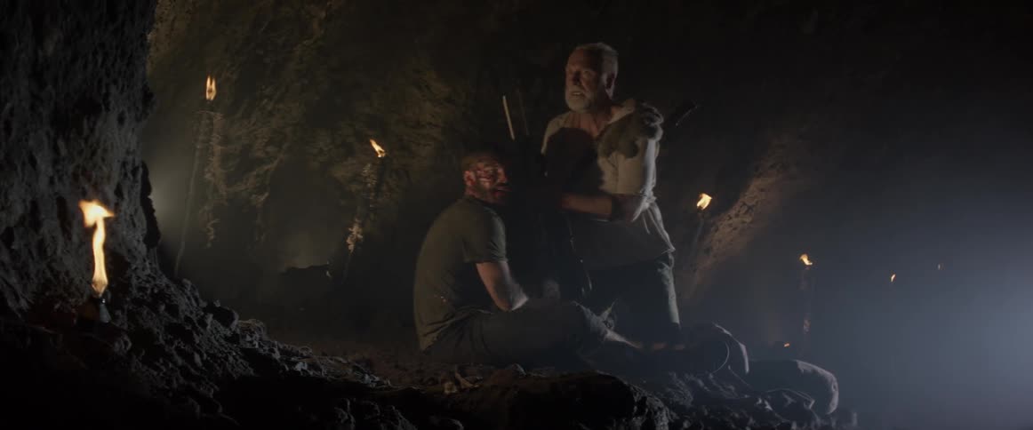 Two men talk in a dark cave