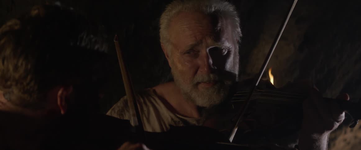 Two people play the violin in a dark cave