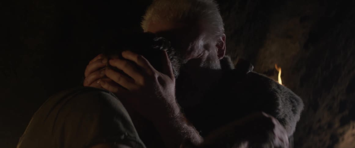 An elderly man consoles a young man in a cave