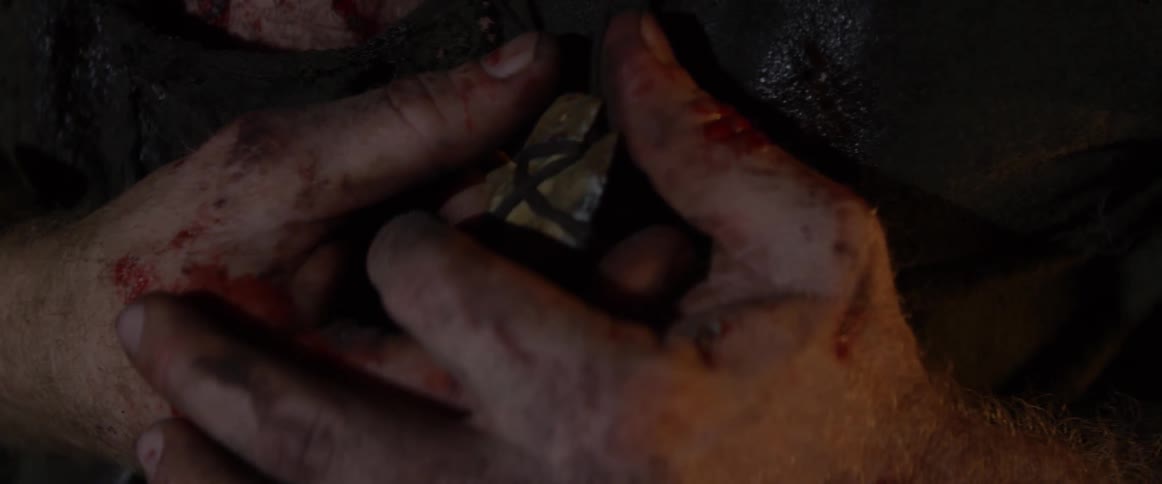 A bloodied man grasps a pendant and holds onto it