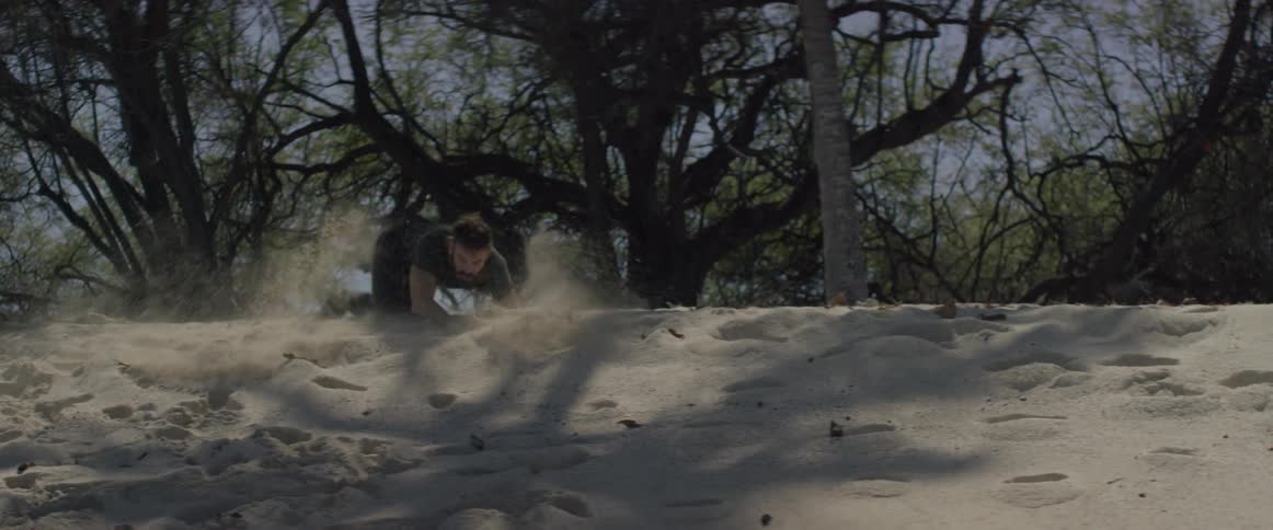 A man falls down while frantically running in the sand
