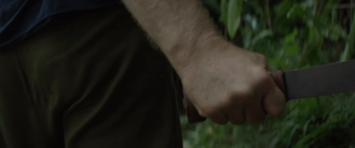 A man carries a machete through a forest tunnel