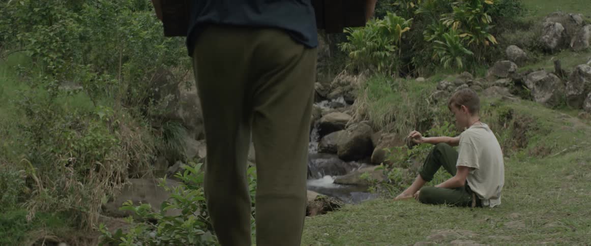 Boy sits next to a rocky stream