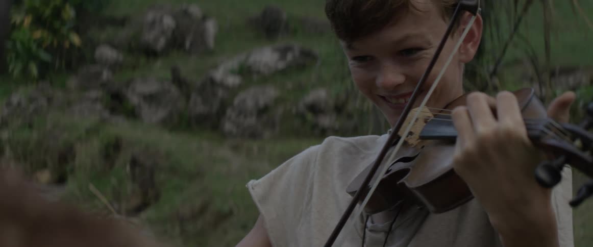 Young boy happily plays the violin outside