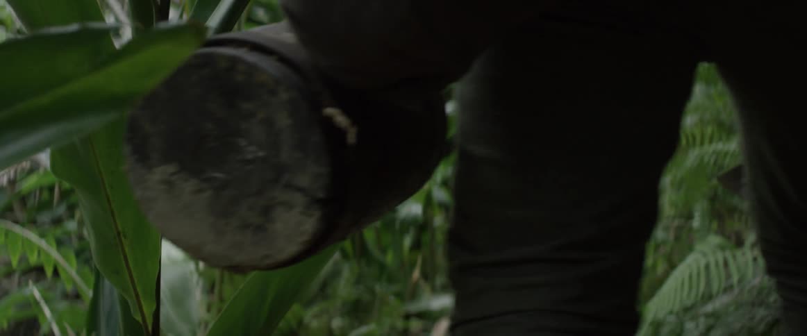 A man carrying a machete and a pack walks through a jungle