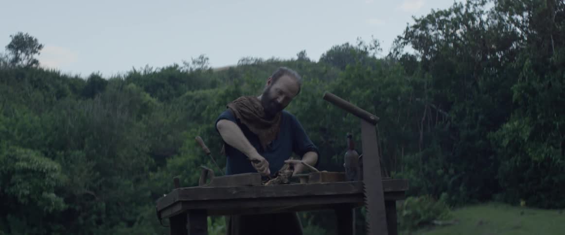 A man whittles wood outside