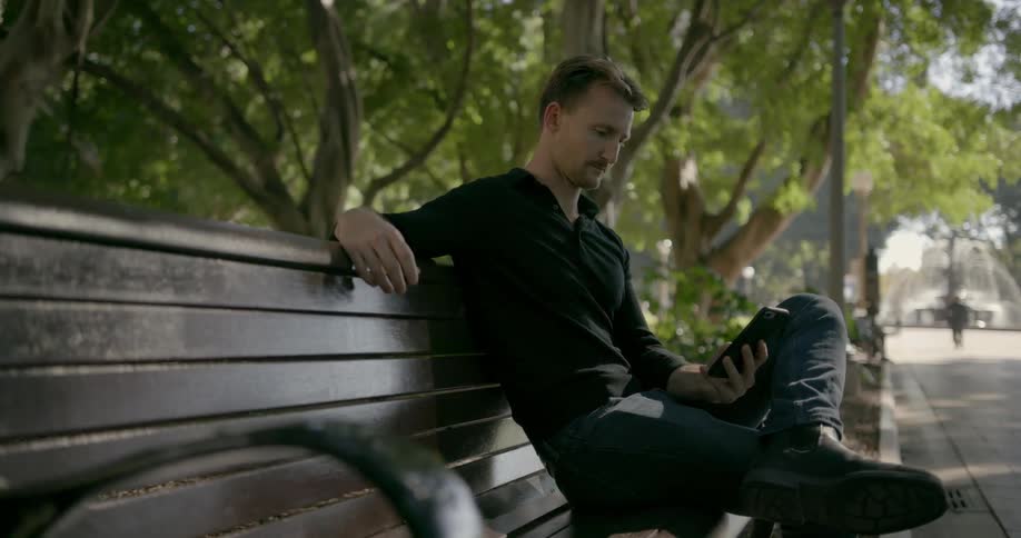 A man looks at his phone while sitting on a park bench