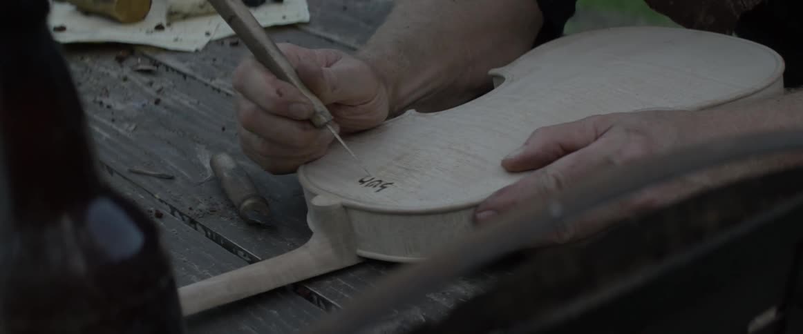 A man is carving writing into the back of a violin
