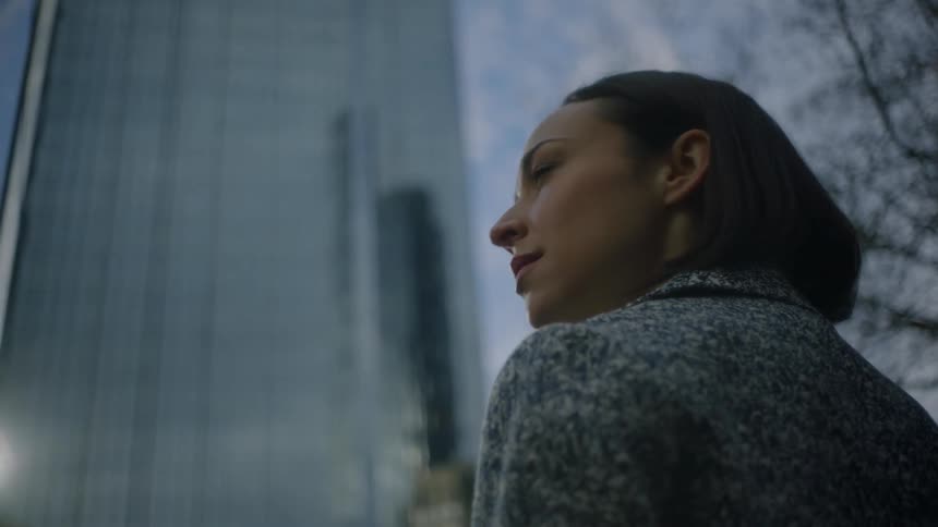 A woman stands near a tall skyscraper