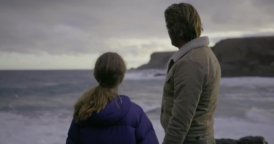 A man stands on the shoreline with a young girl