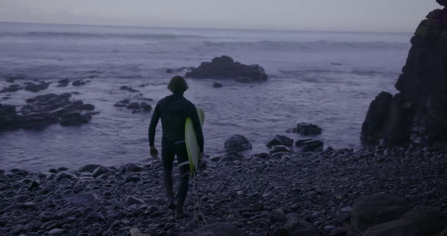 A surfer carries a surfboard approaching the water