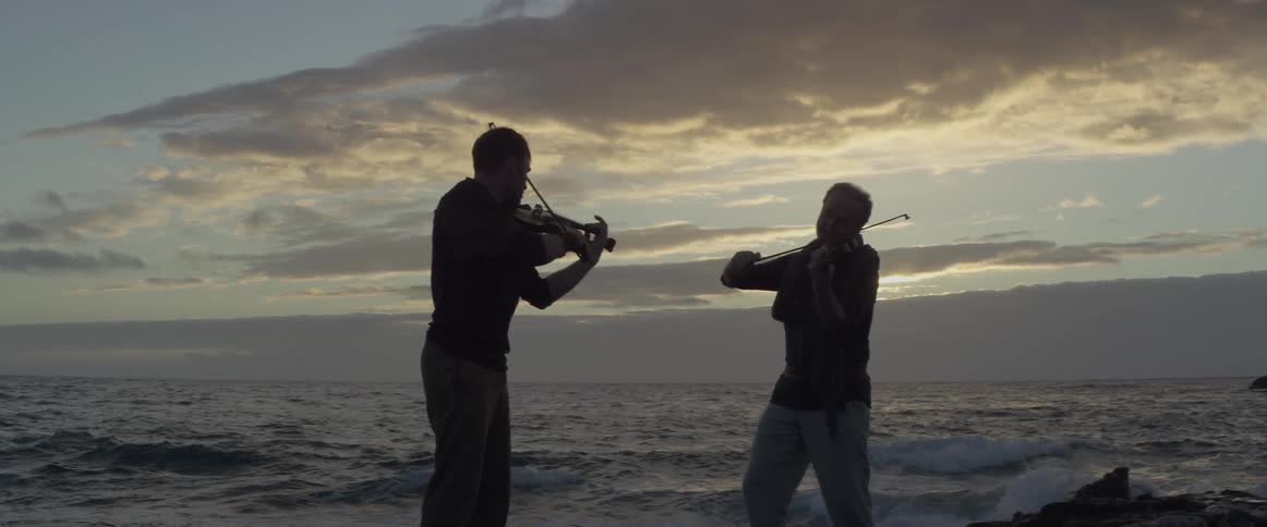 Two men are playing the violin on ocean beach after sunset