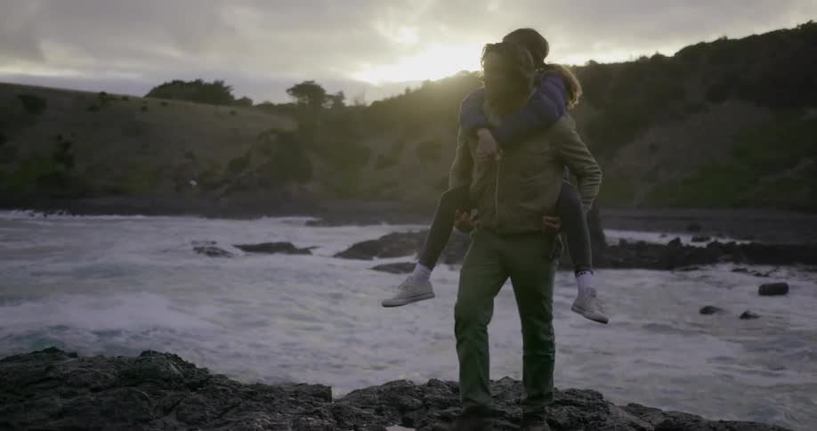 A man gives a girl a piggyback by the stream
