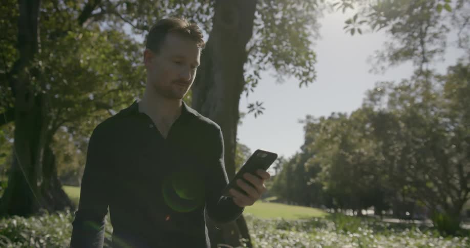 A man walks under trees looking at his cell phone