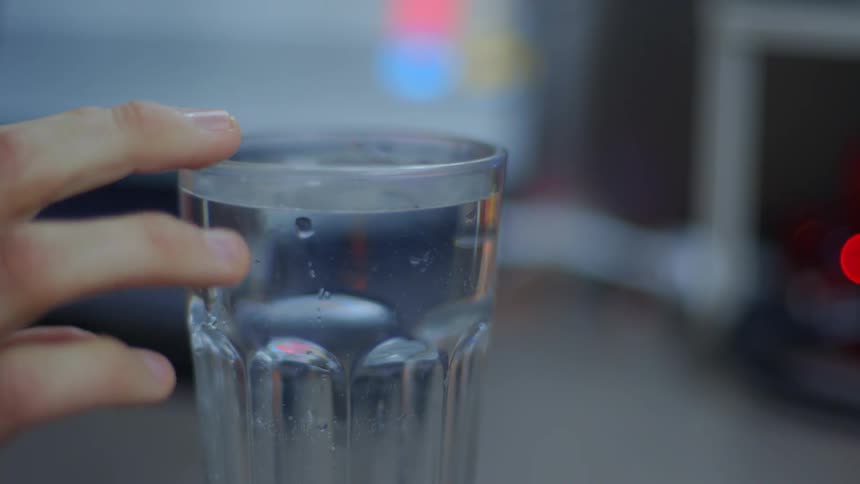 Fingers reach up and into a glass full of water