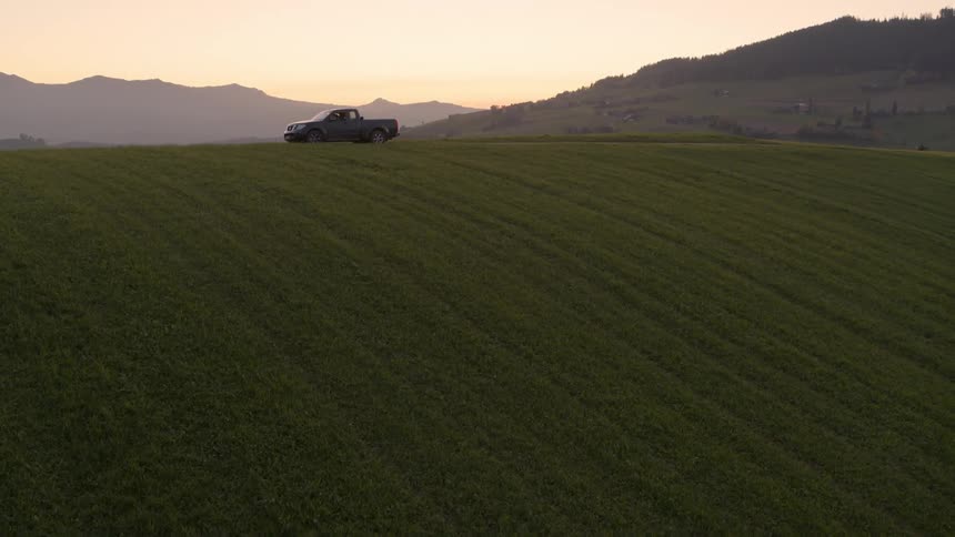 A pickup truck parks on a road near a field at dusk