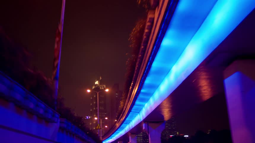 Blue lights illuminate under a city bridge at night