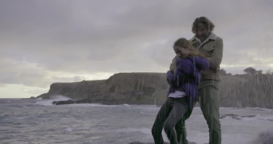 A couple standing by the shore get splashed by a wave