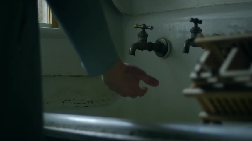 A man puts his hand beneath a dripping faucet in a sink