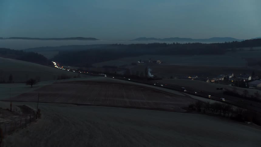 Vehicles travel along a rural highway at dusk