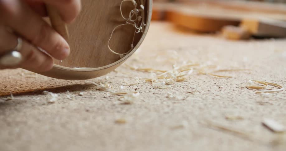 A person picks up a small blade to build a violin