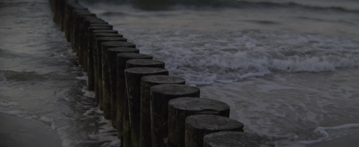 Waves crash into and through wood posts on the beach