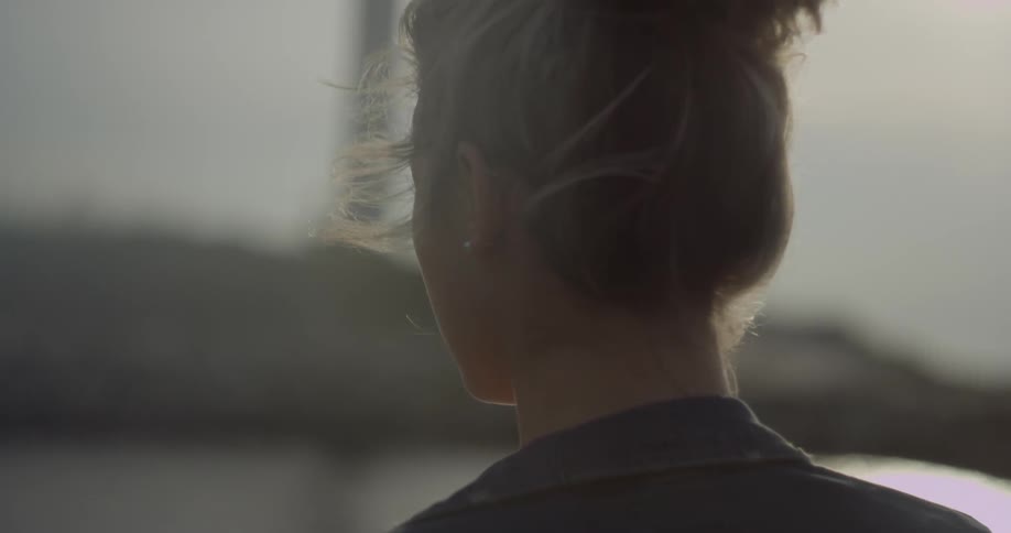 A woman stands outside under the sun as the wind blows her hair
