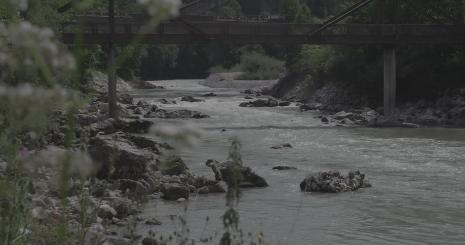 Water in a river rushes beneath a railroad bridge during the day
