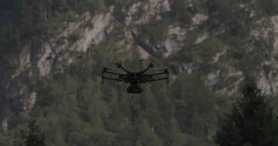 Small drone flies above trees and hill