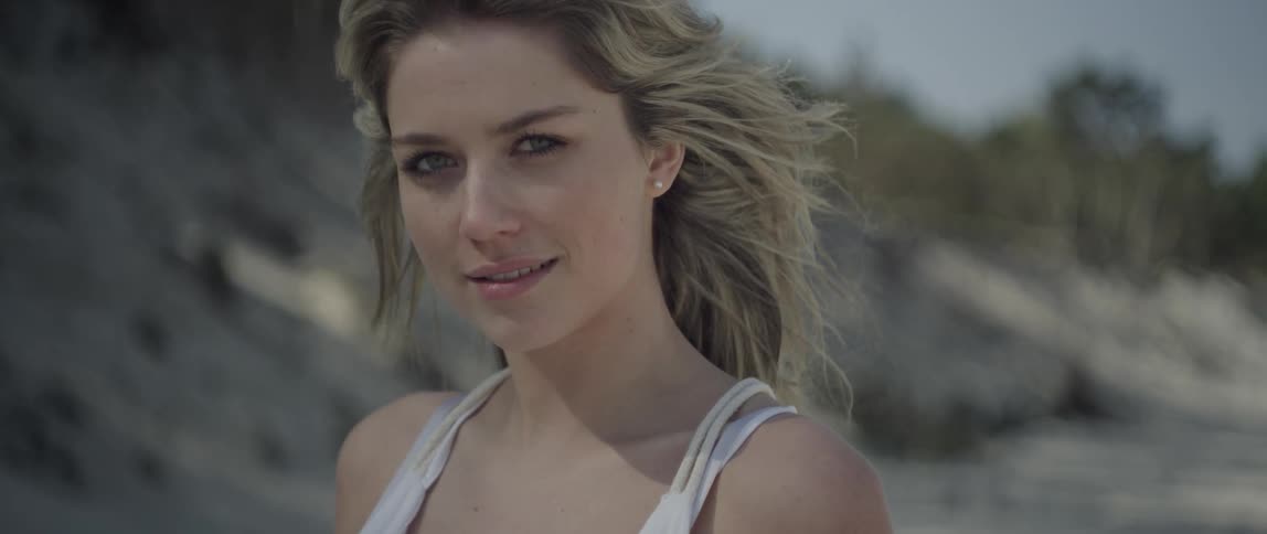 A woman with her hair blowing in the wind is smirking at the camera
