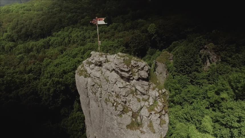 A large mountain with a flag on top is filmed by a drone