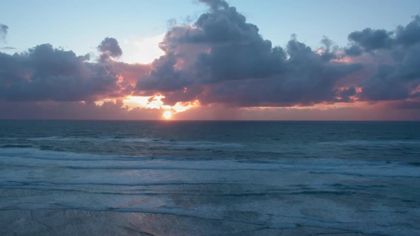 The sunset is being filmed by a drone on the beach