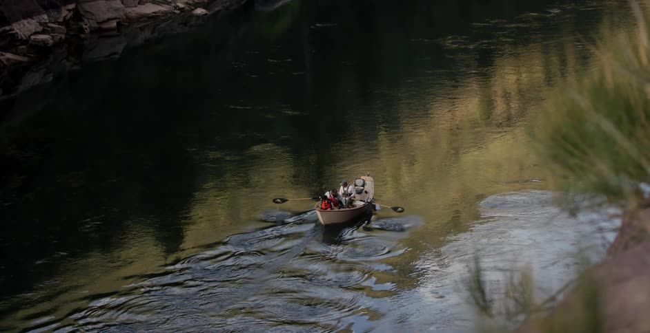 Two people paddle a boat down a stream
