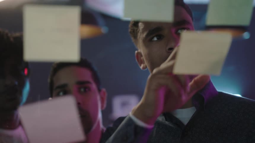 Workers in an office read post it notes on a window together