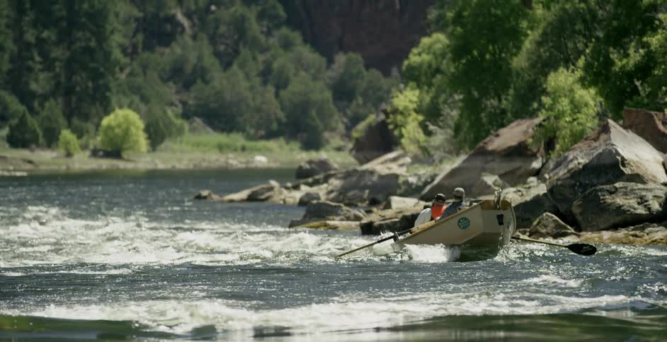 Two people paddle a boat down a fast flowing river