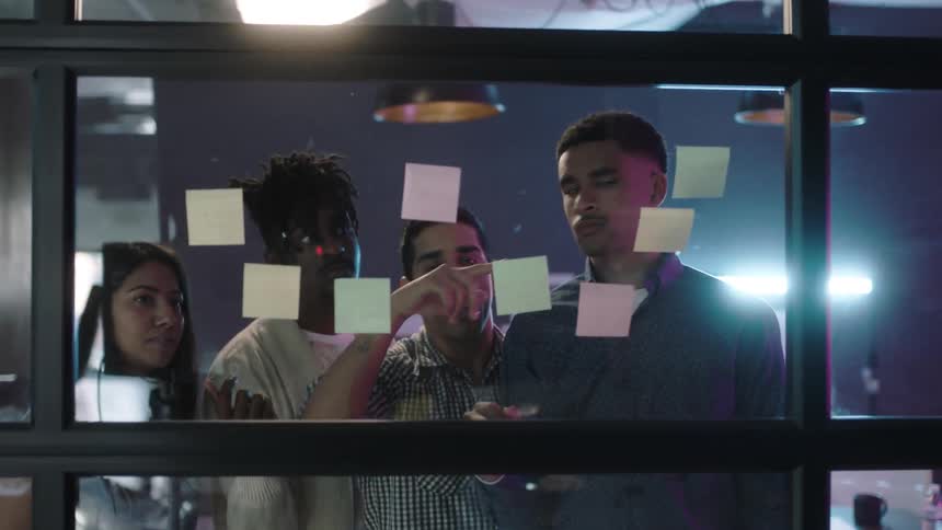 Men and women put sticky notes on a window and discuss them